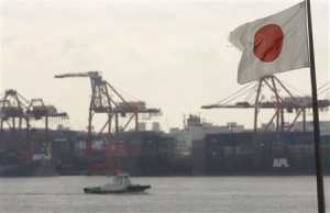 A Japanese flag flutters in front of a shipping container area, at a port in Tokyo